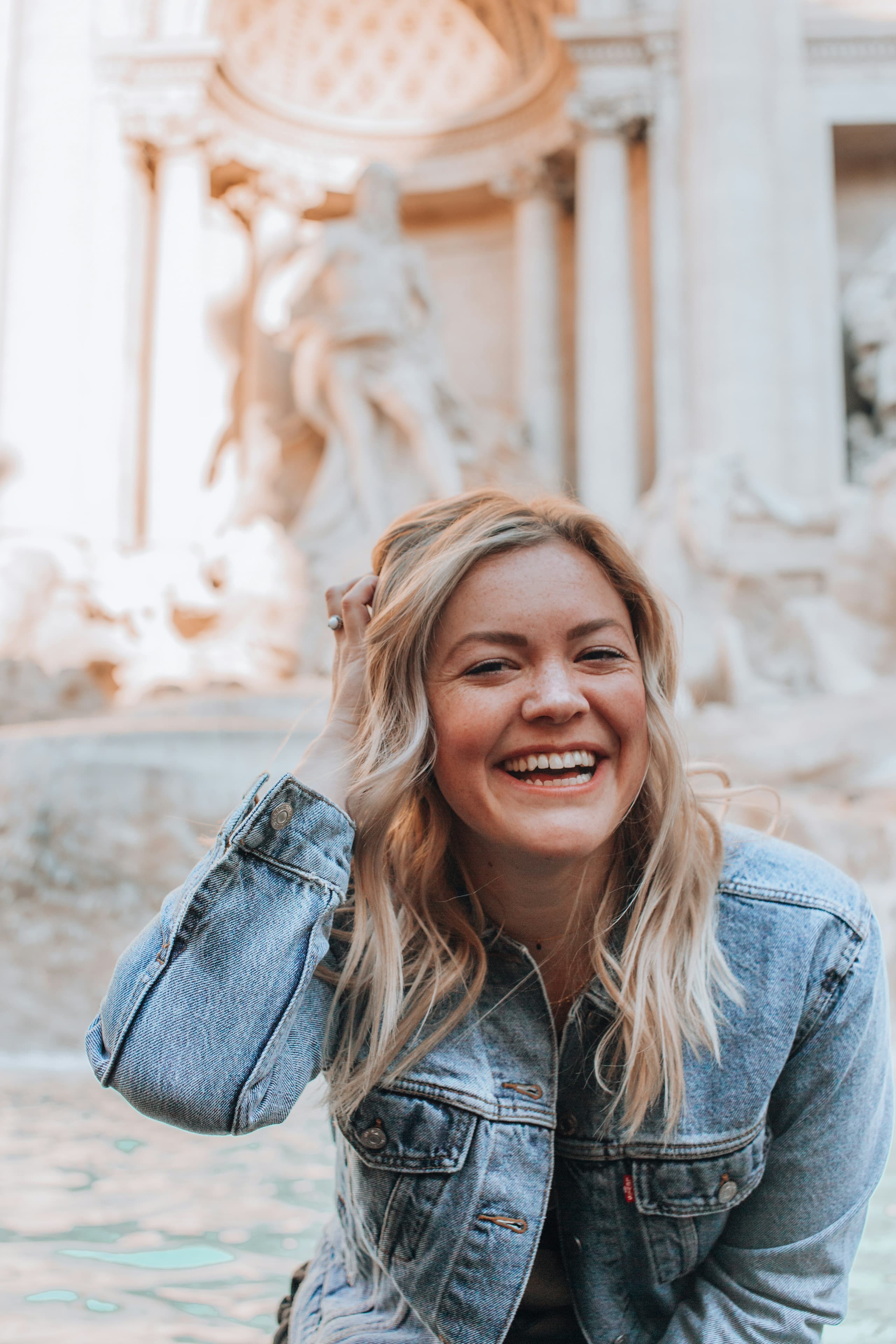 A woman smiling outdoors beside a stone fountain